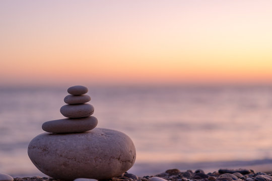 Balanced stack of smooth stones on a shore at soft sunset, sea and sky blurred in the background